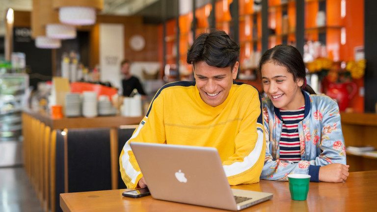 Teenage brother and sister looking at laptop in cafe together 