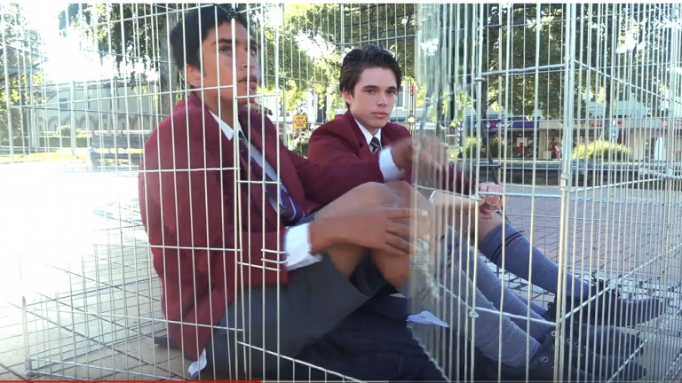 James and Ishan of St. John's College Hastings sit in a cage in protest at prison conditions in Hastings central square