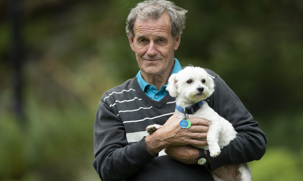 An older man holding a small white dog in his arms.